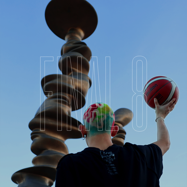 Una persona con i capelli colorati gioca le final 8 di basket con di fronte una scultura astratta di Torino